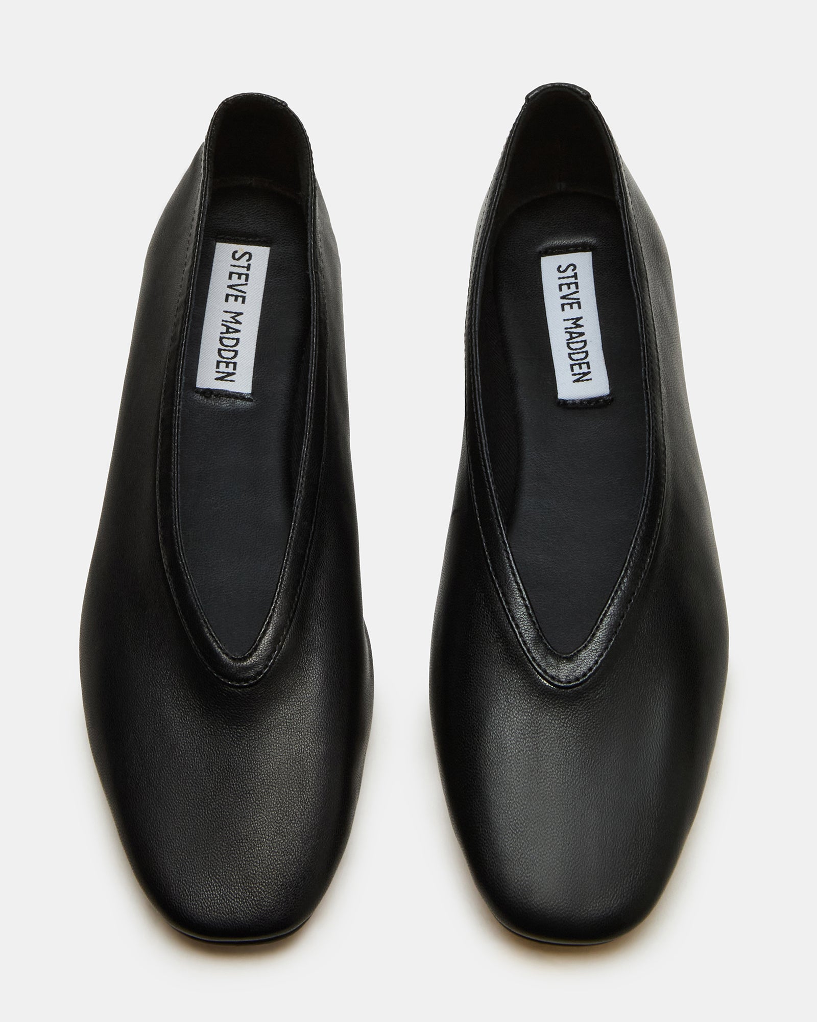 Side view of black leather square toe ballet flats on a wooden floor.