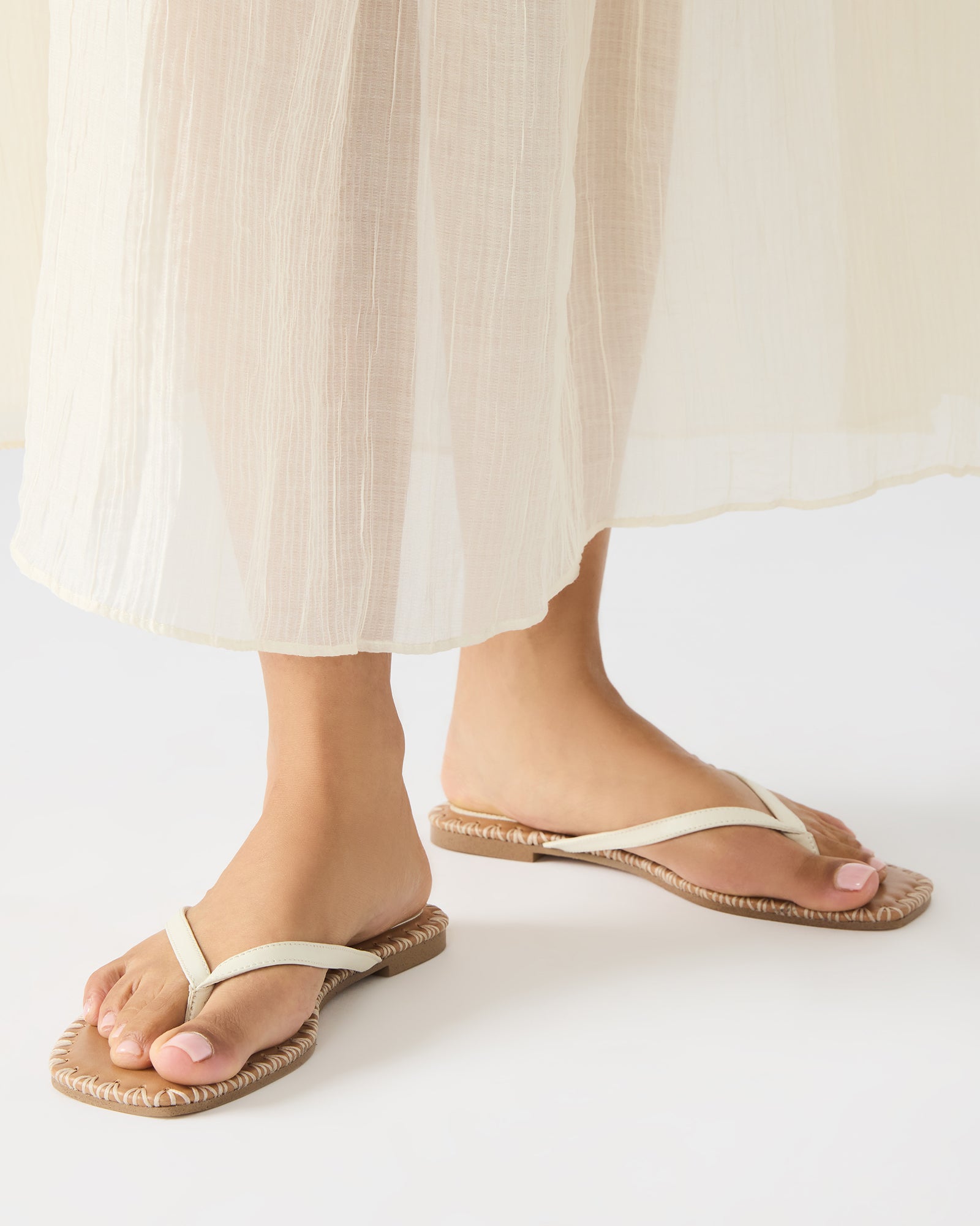 Top-down perspective of square toe thong sandals on wooden floor