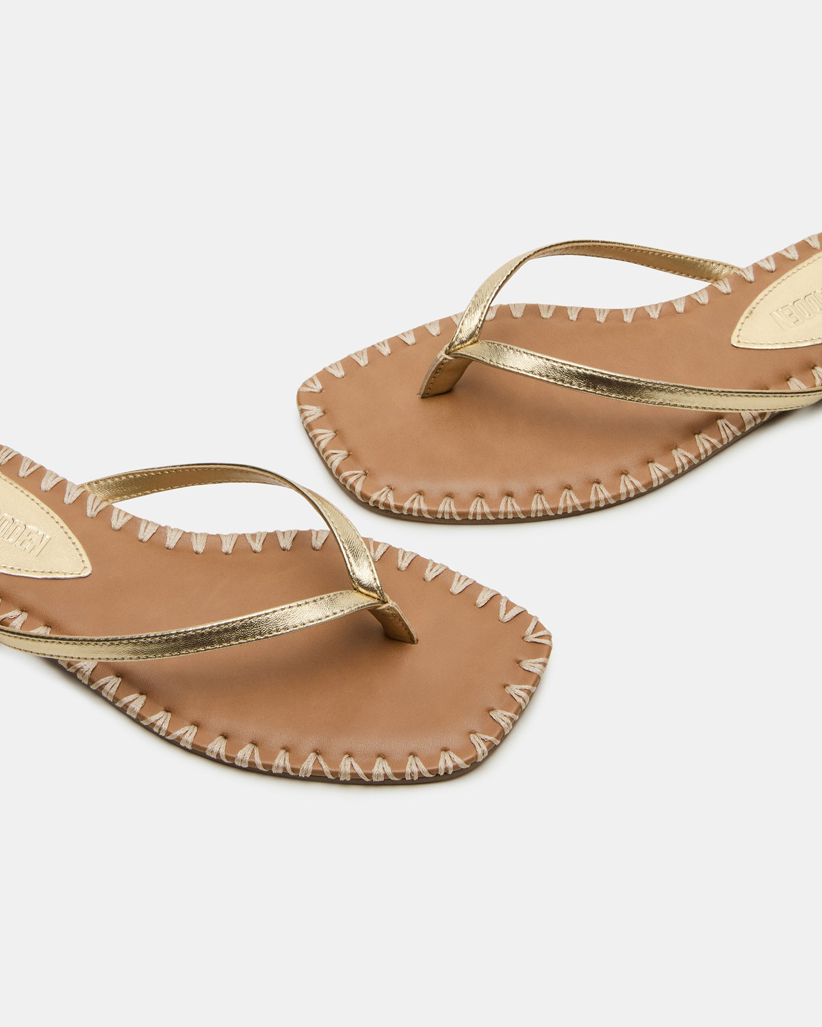 Gold leather square toe sandals with thong strap on a model’s feet