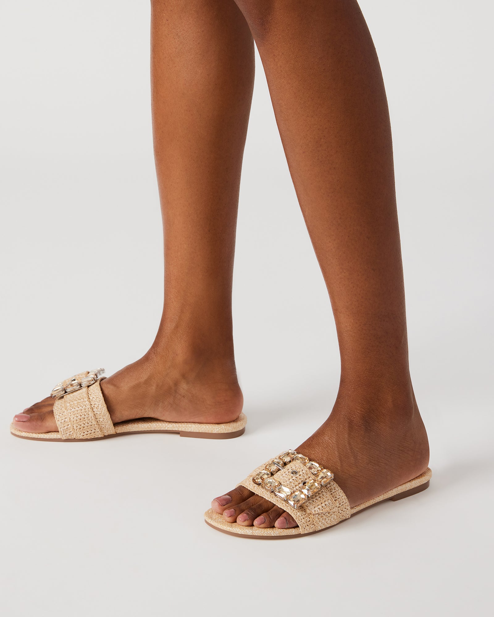 Lifestyle image of woman wearing slide sandals while walking outdoors on sunlit pathway.