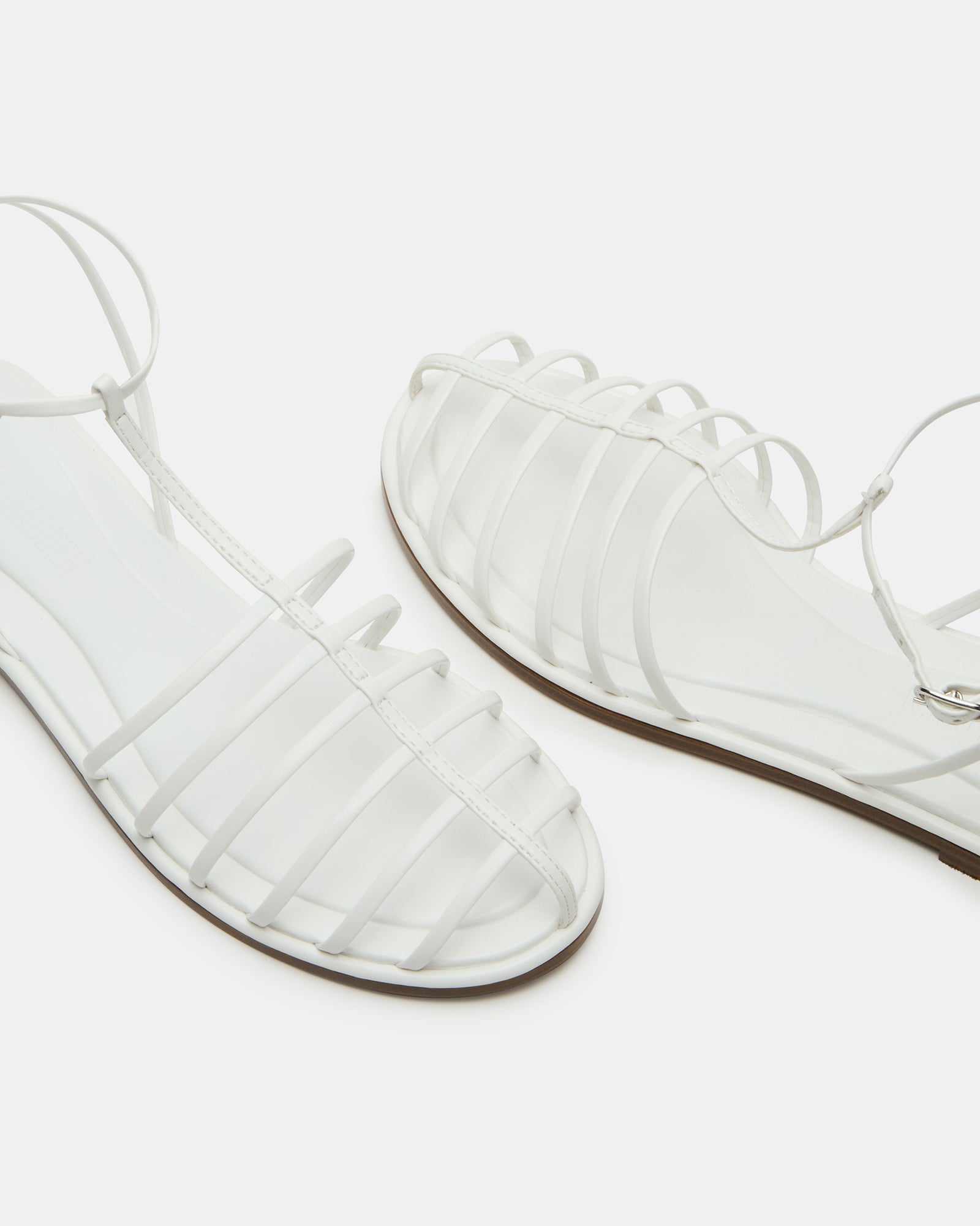 Side view of white strappy sandals showing secure ankle strap and sleek silhouette