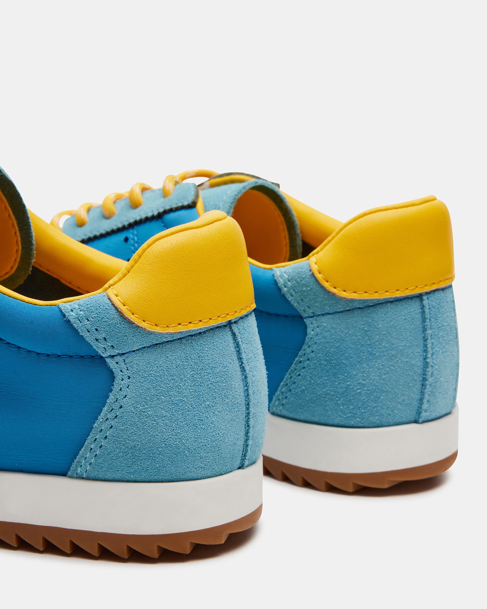Side view of white sneakers with blue/yellow accents, styled with jeans