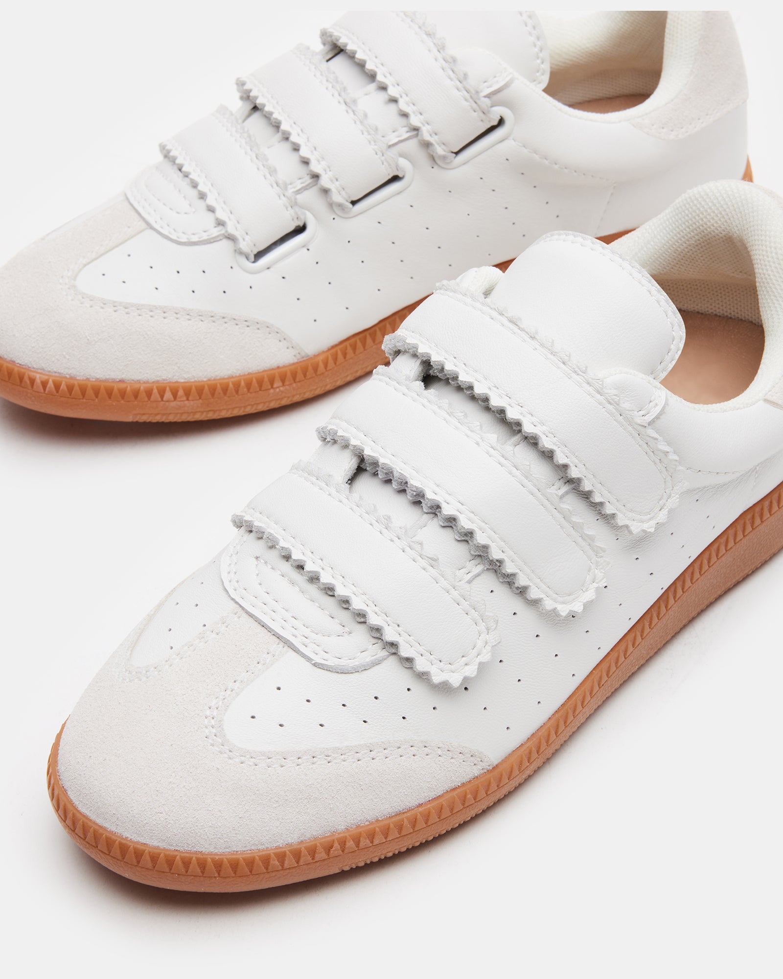 A pair of Momentum White Velcro sneakers on a wooden floor, highlighting their sleek design.