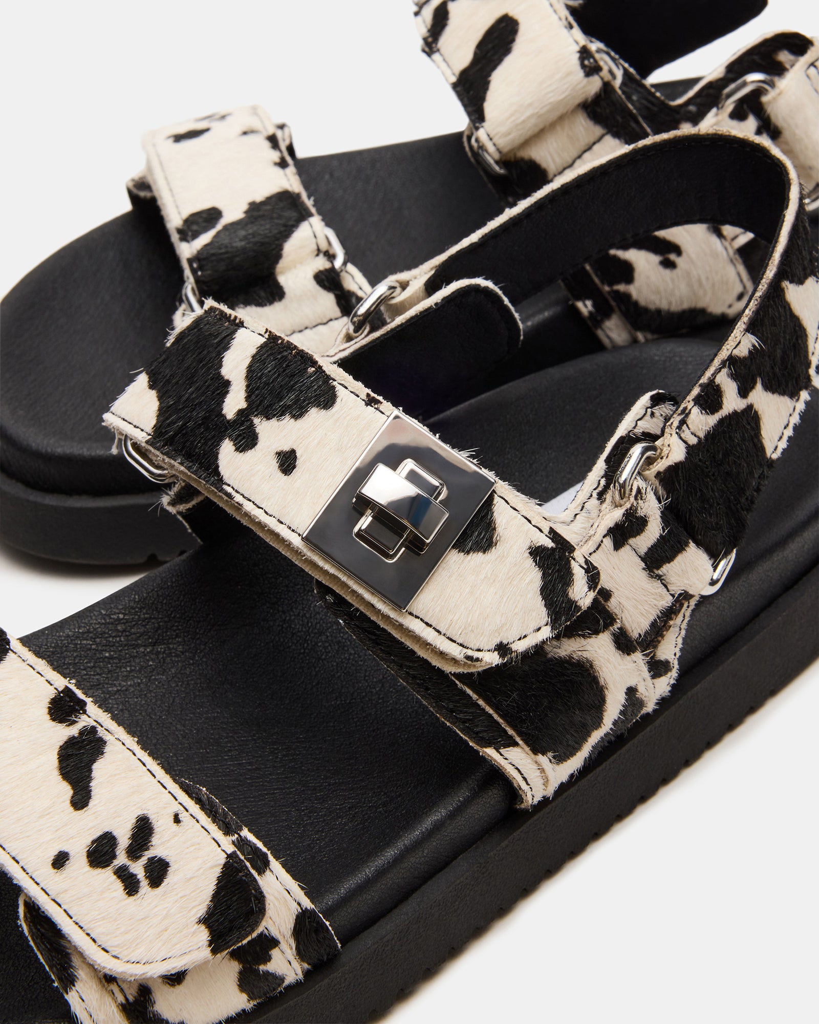 Side view of MONA black cow print leather flatform sandals on a model’s feet