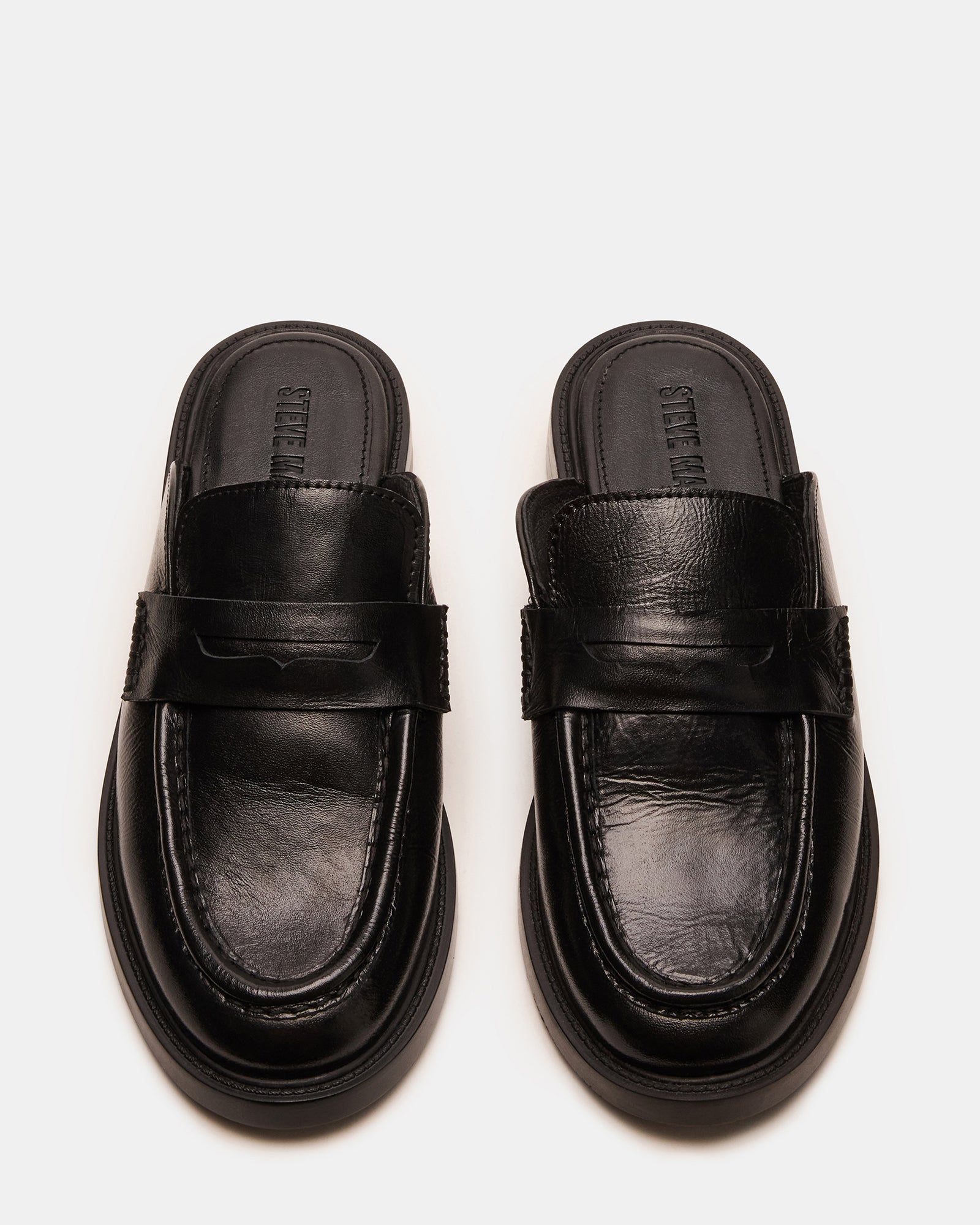 Front angle of black leather flat mules against marble backdrop