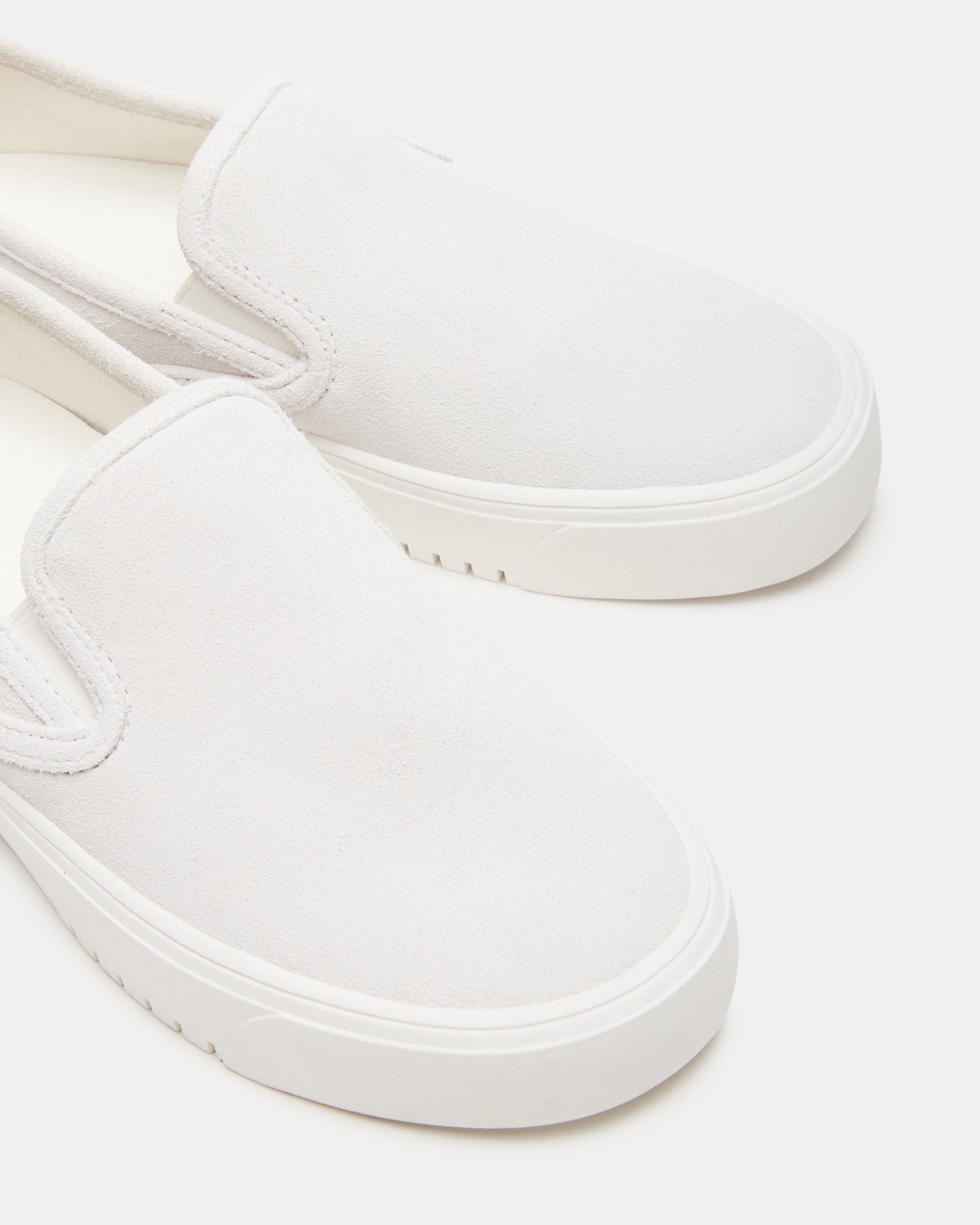 Side view of low-top sneakers in white suede worn with cuffed jeans