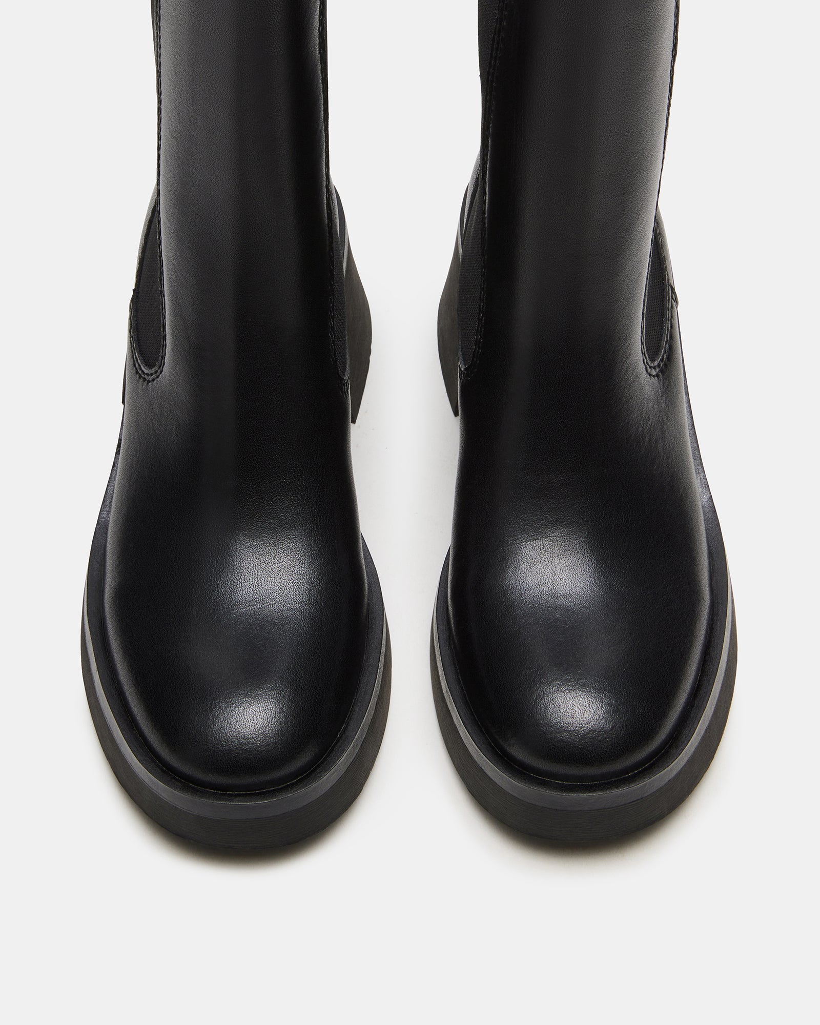 Side profile of black chelsea boots with rounded toe on hardwood floor