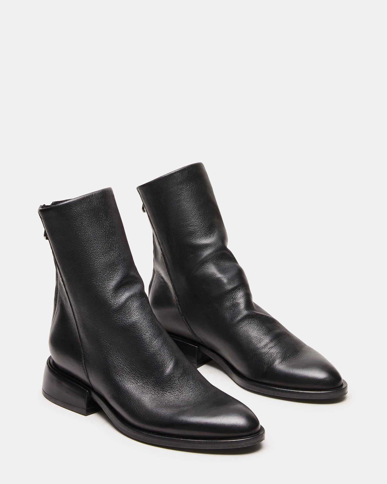 Close-up of inside zipper on black ankle boots against wood floor background.