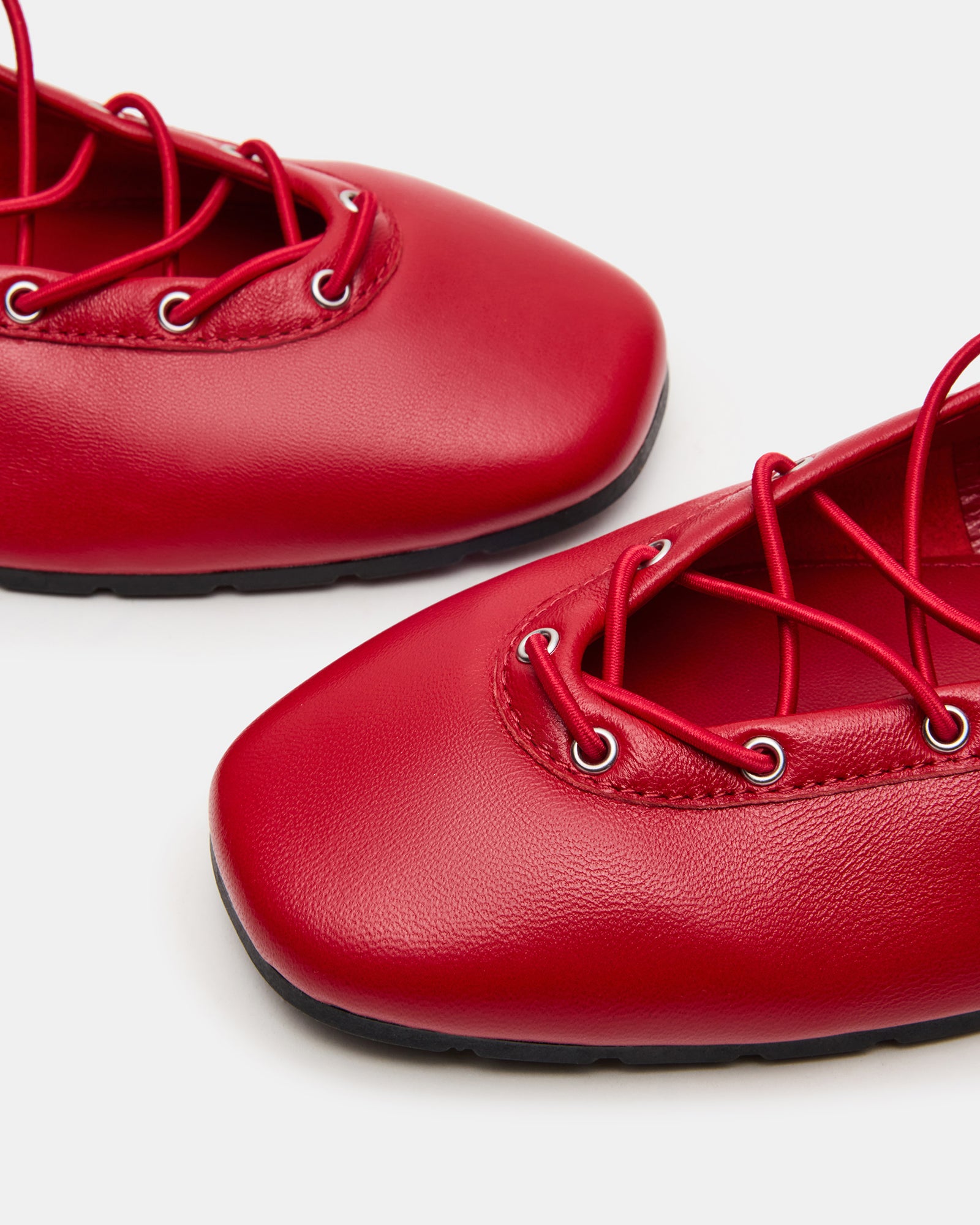 Red leather ballet flats with square toe and ankle ties on a stylish woman’s feet