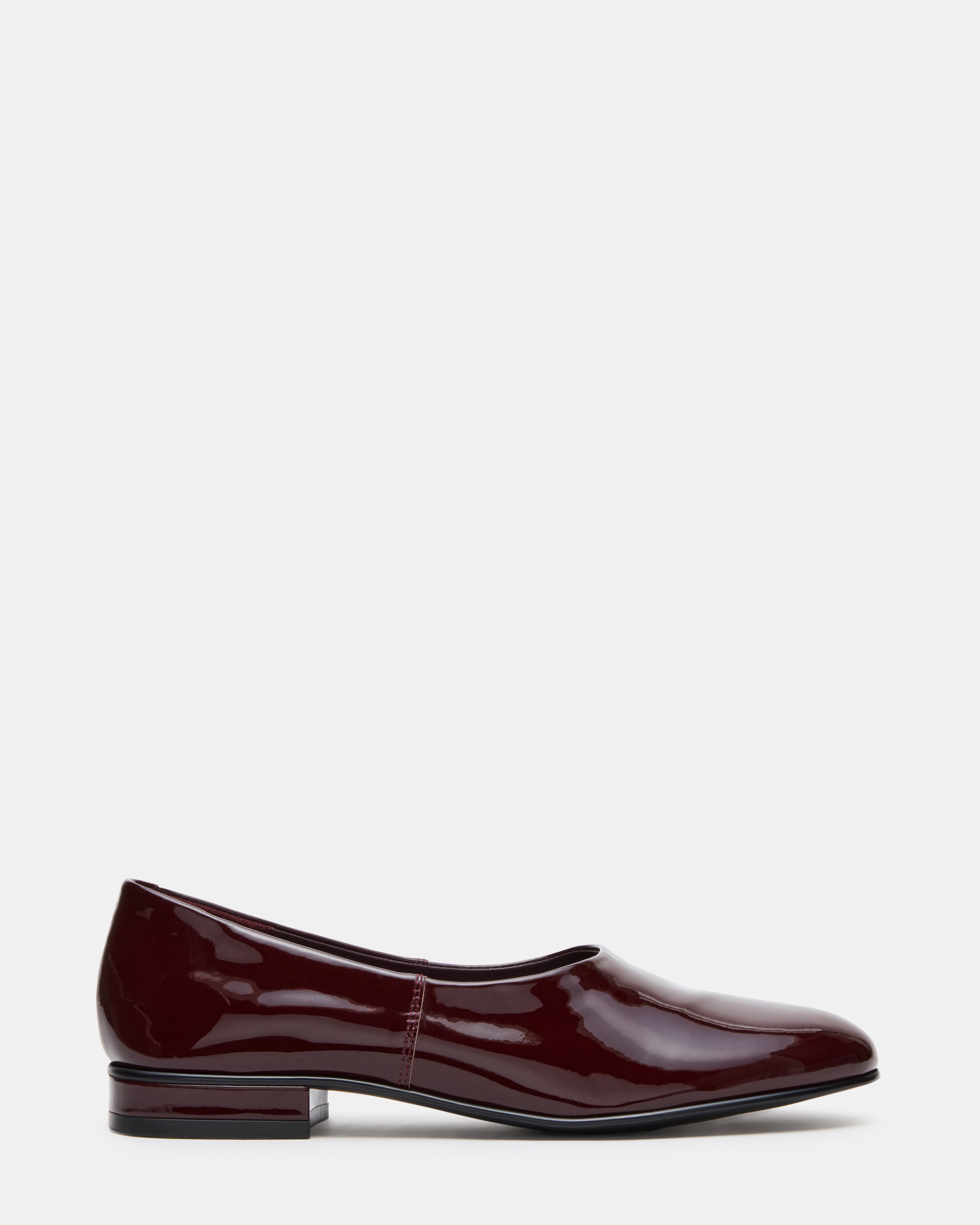 Side view of burgundy patent leather ballet flats on a stylish floor.