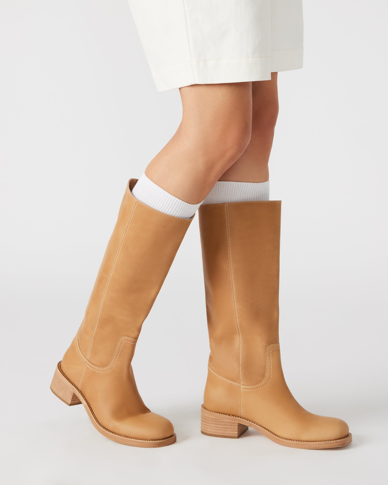 Brown knee high boots styled with jeans, shown walking on pavement