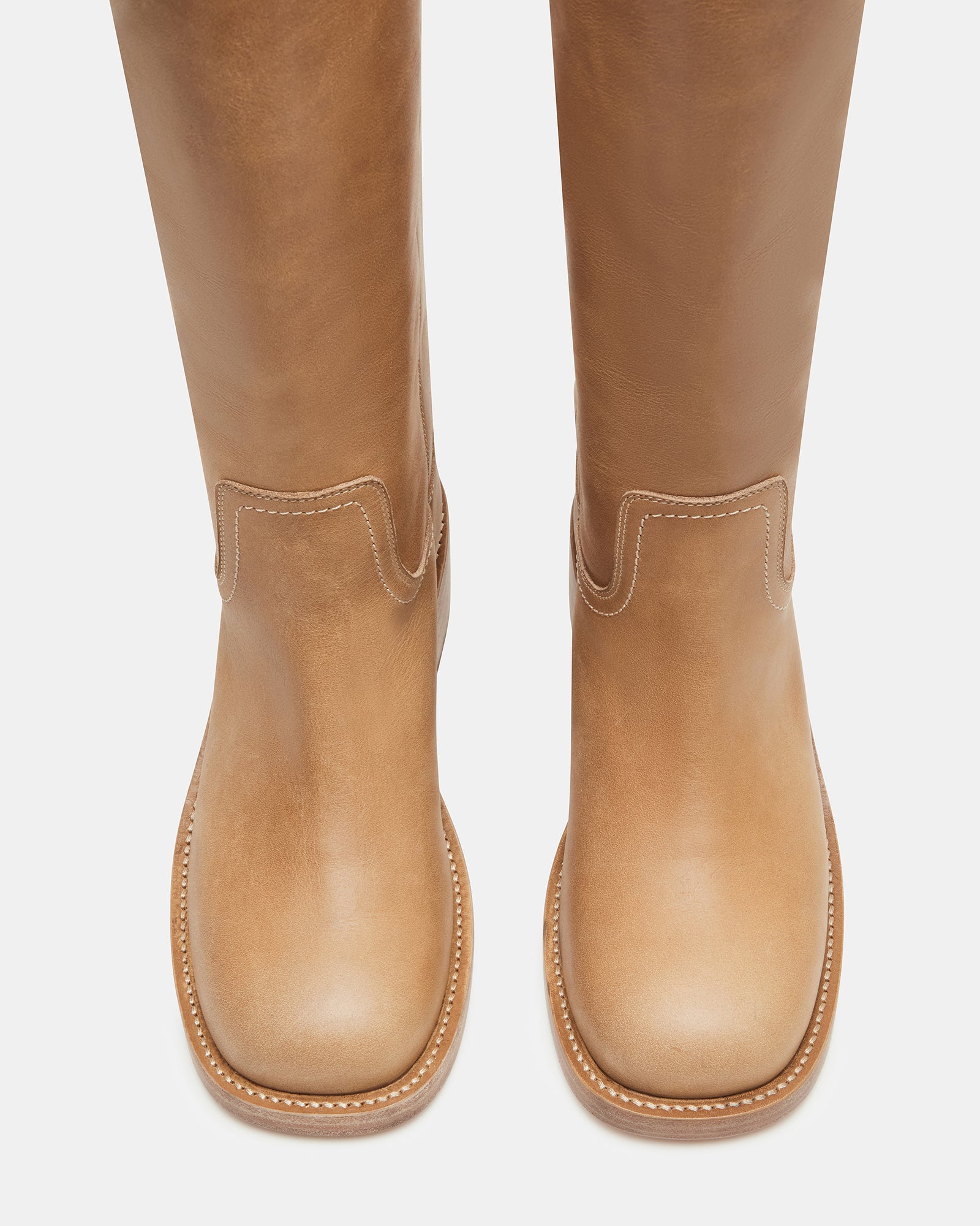 Brown knee high boots styled with jeans, shown walking on pavement