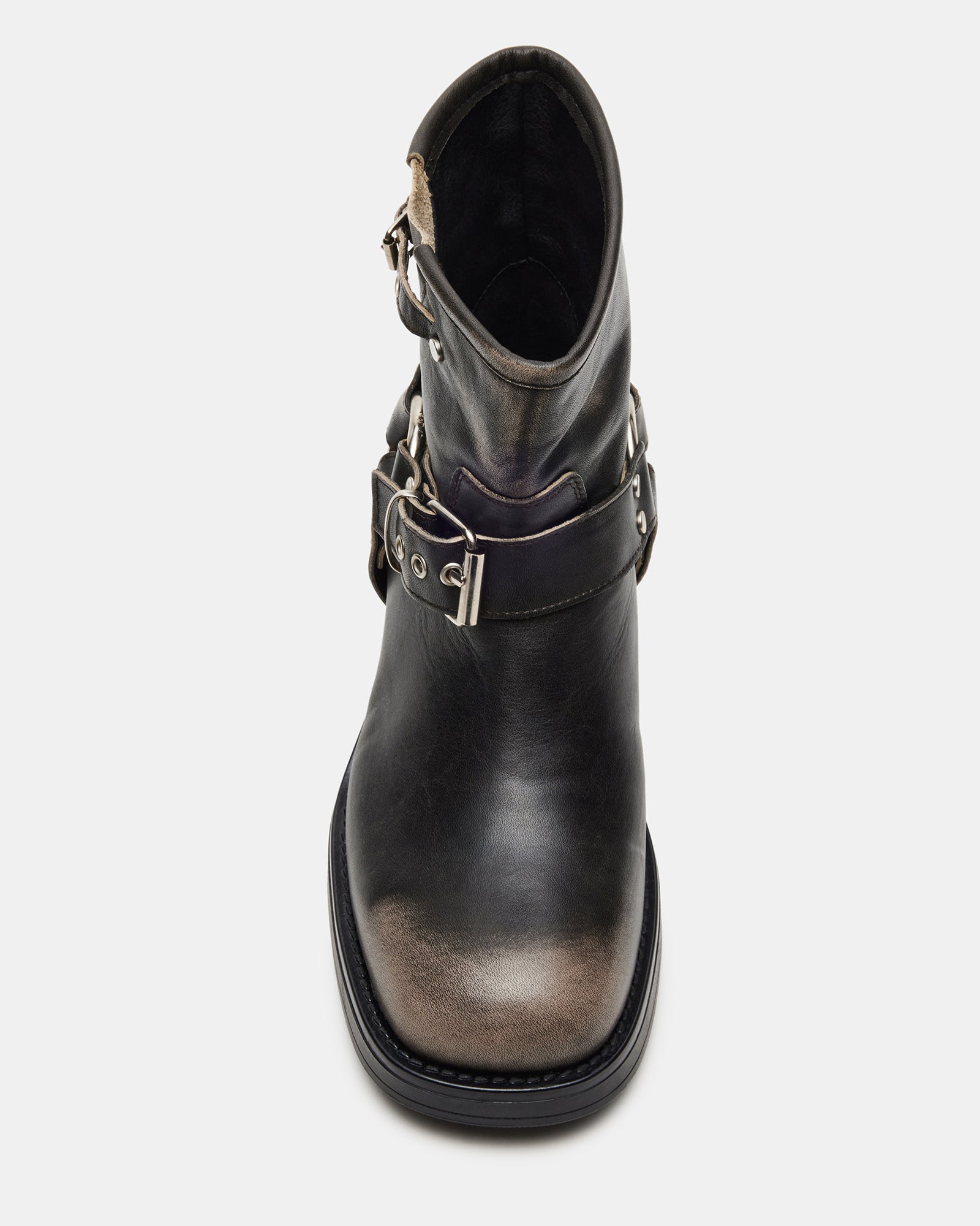 Side view of black ankle boots with buckles on a city sidewalk.
