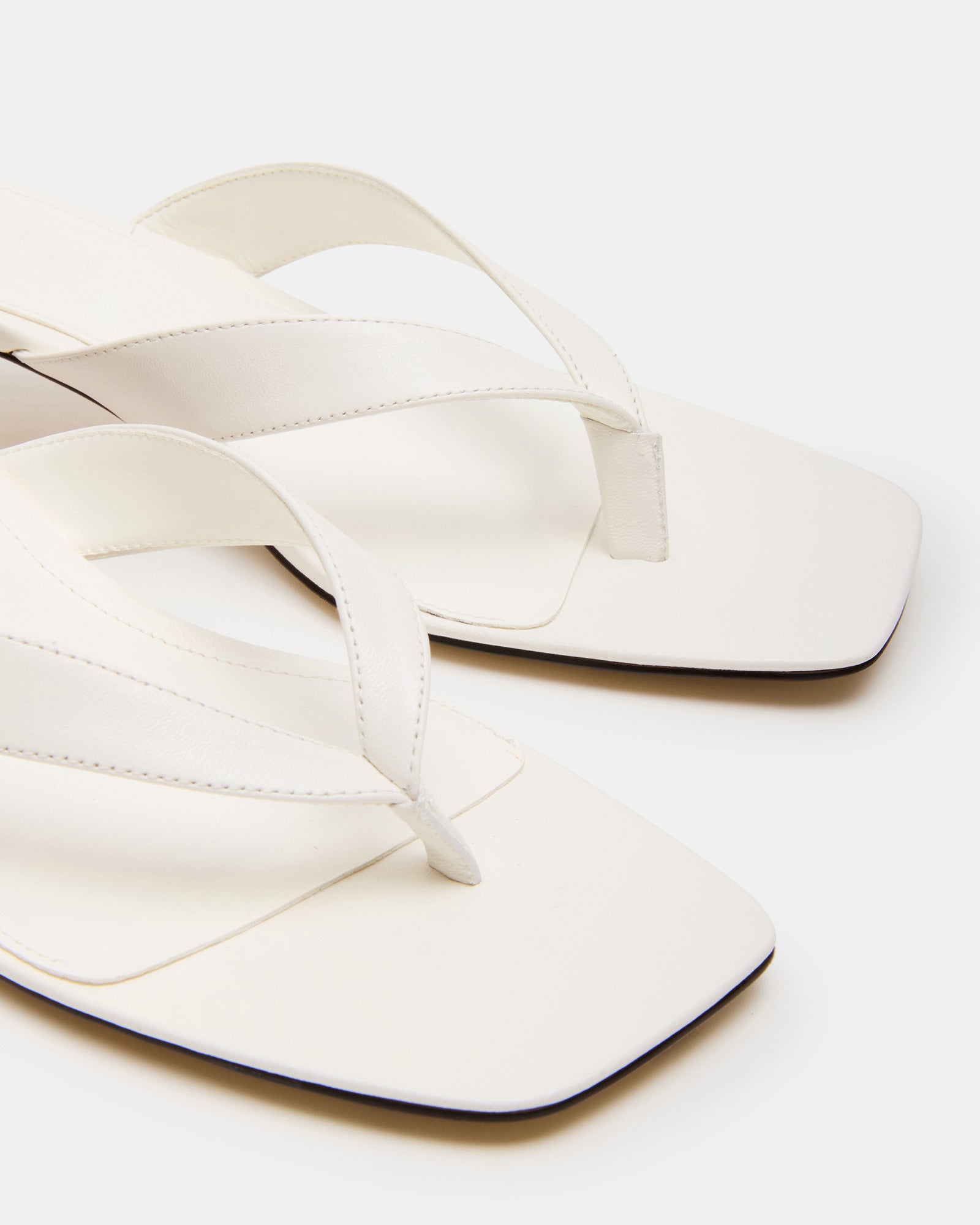 White leather shoes with kitten heels and thong strap, styled for formal occasions
