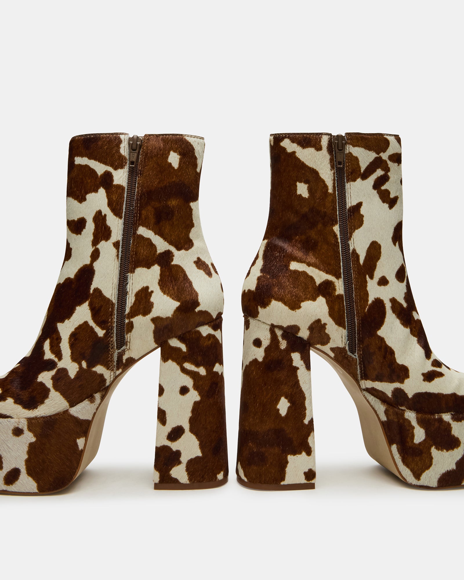 Model wearing brown cow print ankle boots paired with denim and dress