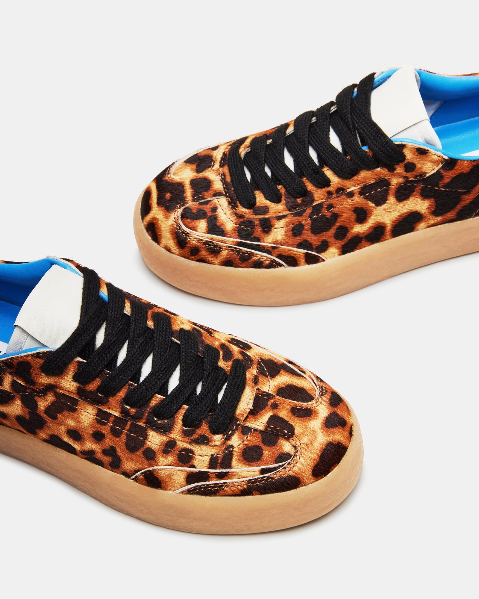 Side profile of white sneakers with leopard accents, shown with urban streetwear