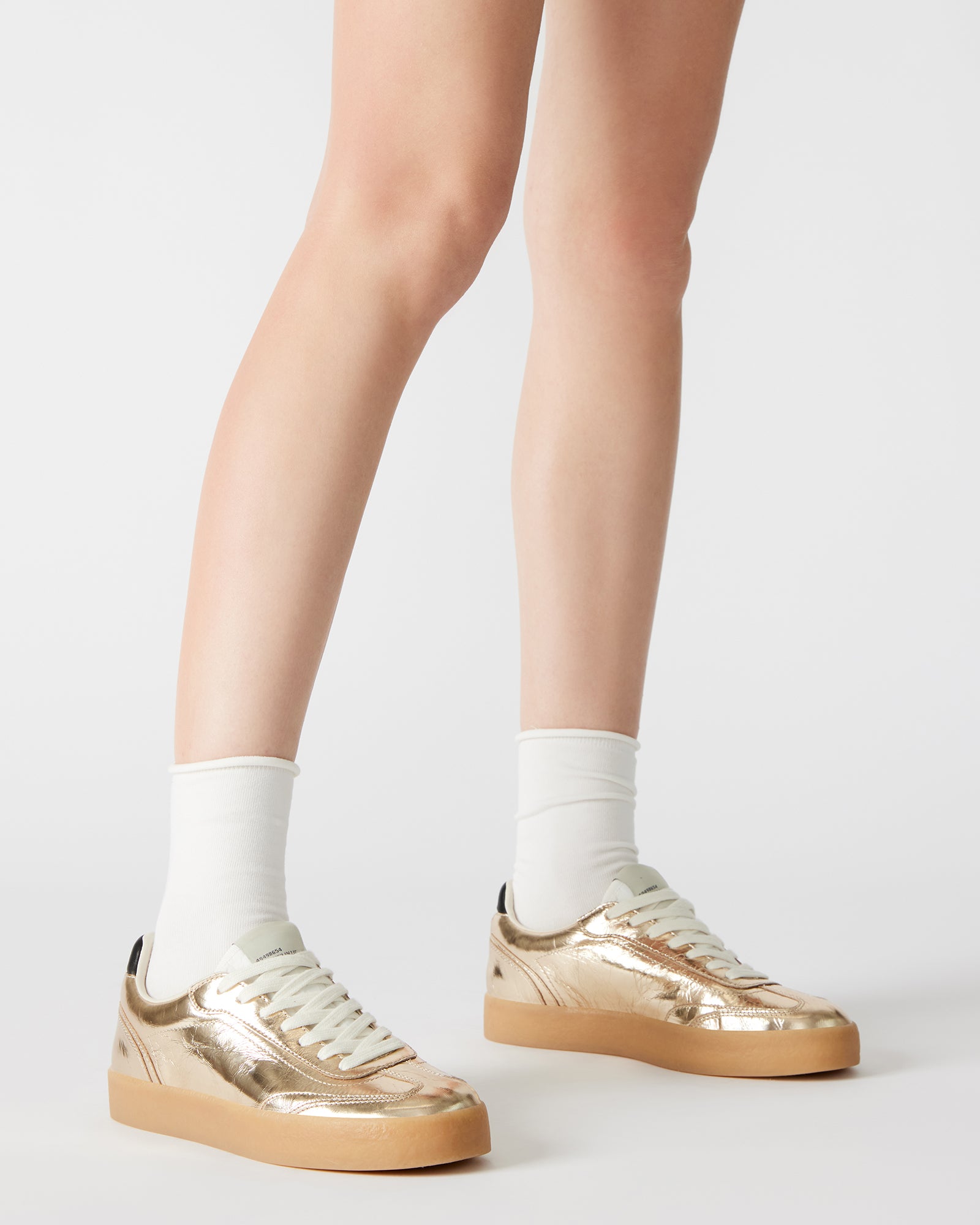 Close-up of lace-up design and patent leather texture on TUX Gold sneakers